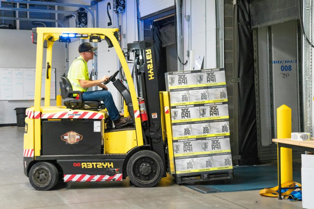 pexels-photo-1267324-1267324 A worker drives a Hyster forklift moving Joe IPA boxes in a warehouse.